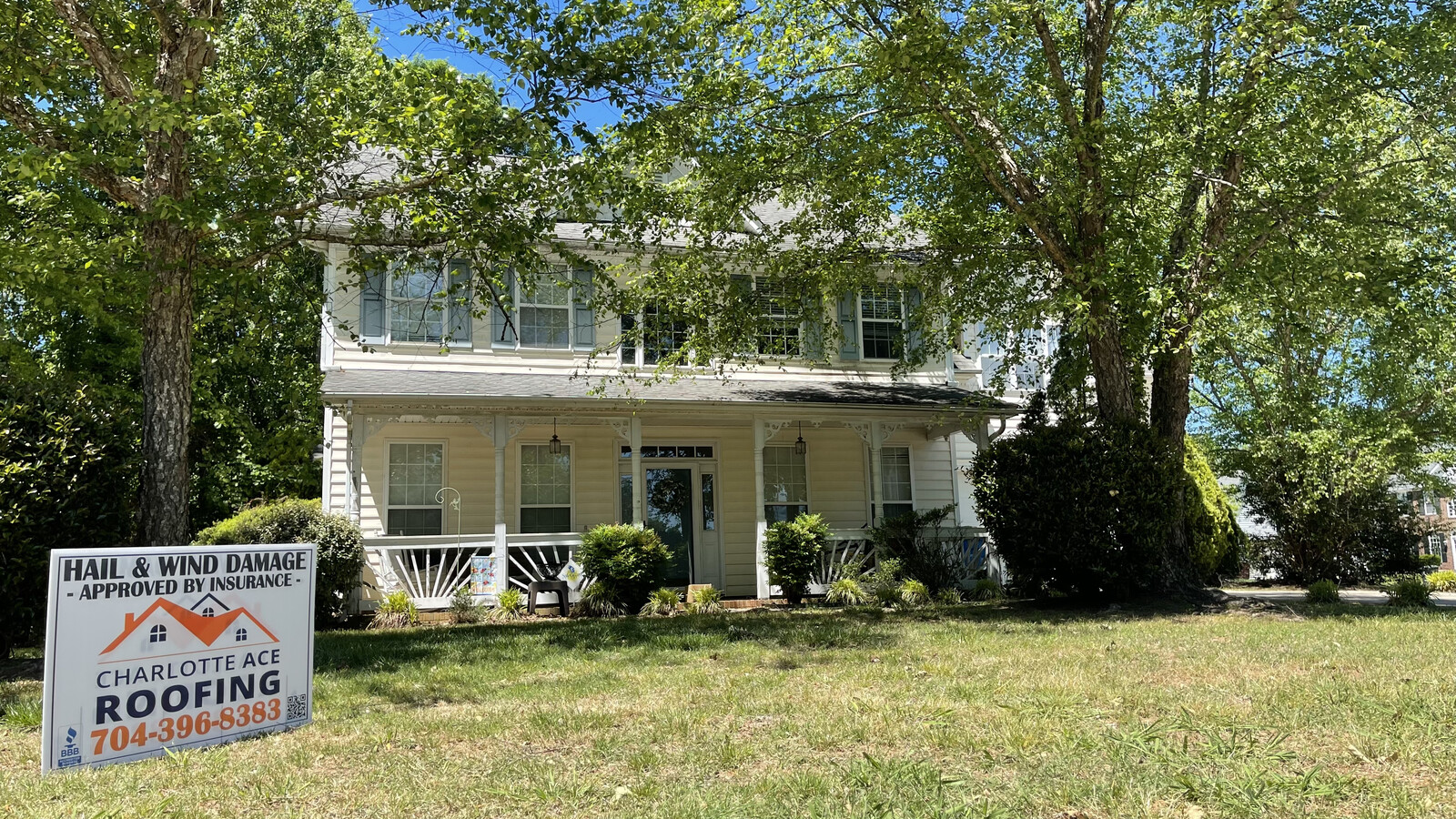 Completed roof replacement on a yellow Victorian-style two-story home with wraparound porch in Belmont, NC \u2014 Charlotte Ace Roofing yard sign visible