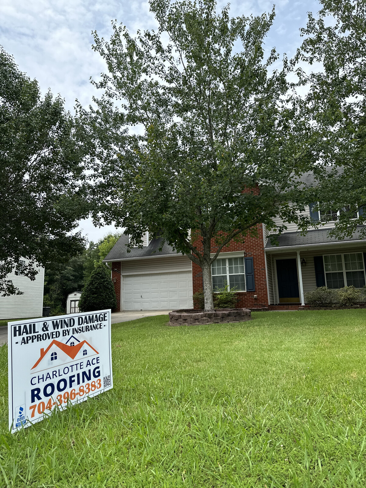 Two-story brick and siding home in Cotswold area Charlotte with Charlotte Ace Roofing 'Hail and Wind Damage Approved by Insurance' yard sign