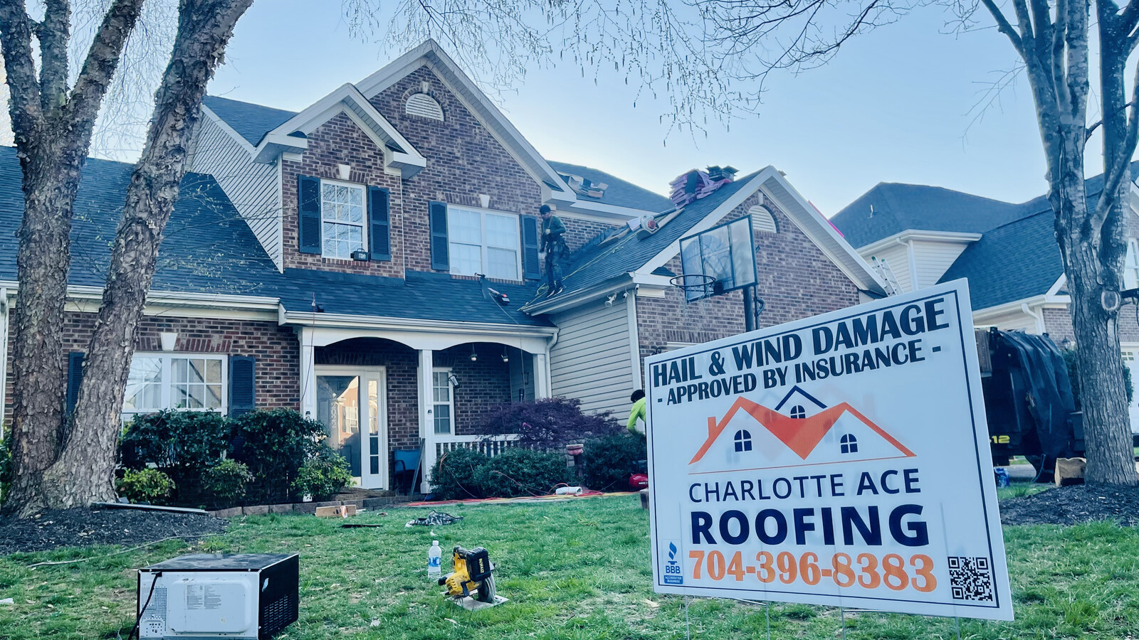 Roof replacement installation in progress on a brick executive home in Stallings, NC — Charlotte Ace Roofing crew laying new shingles, hail and wind damage approved by insurance yard sign in foreground