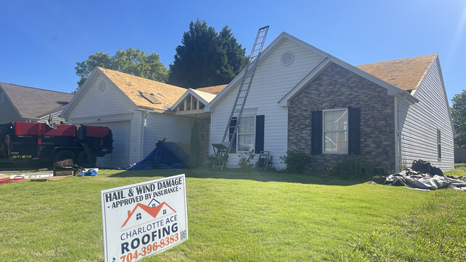 Roof tear-off in progress on a stone-and-vinyl ranch home in Stallings, NC — Charlotte Ace Roofing dump truck in driveway, deck stripped to bare wood, new shingles staged on roof